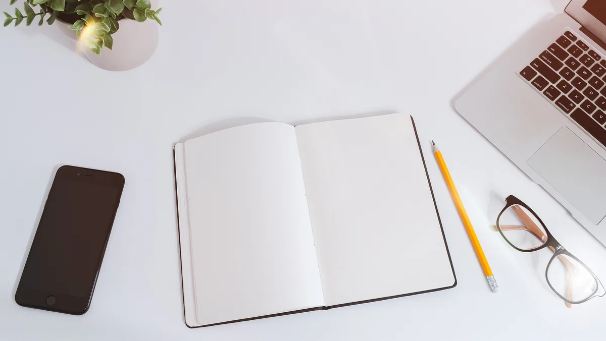 Smartphone, aufgeschlagenes Notizbuch und Notebook auf einem hellen Arbeitstisch